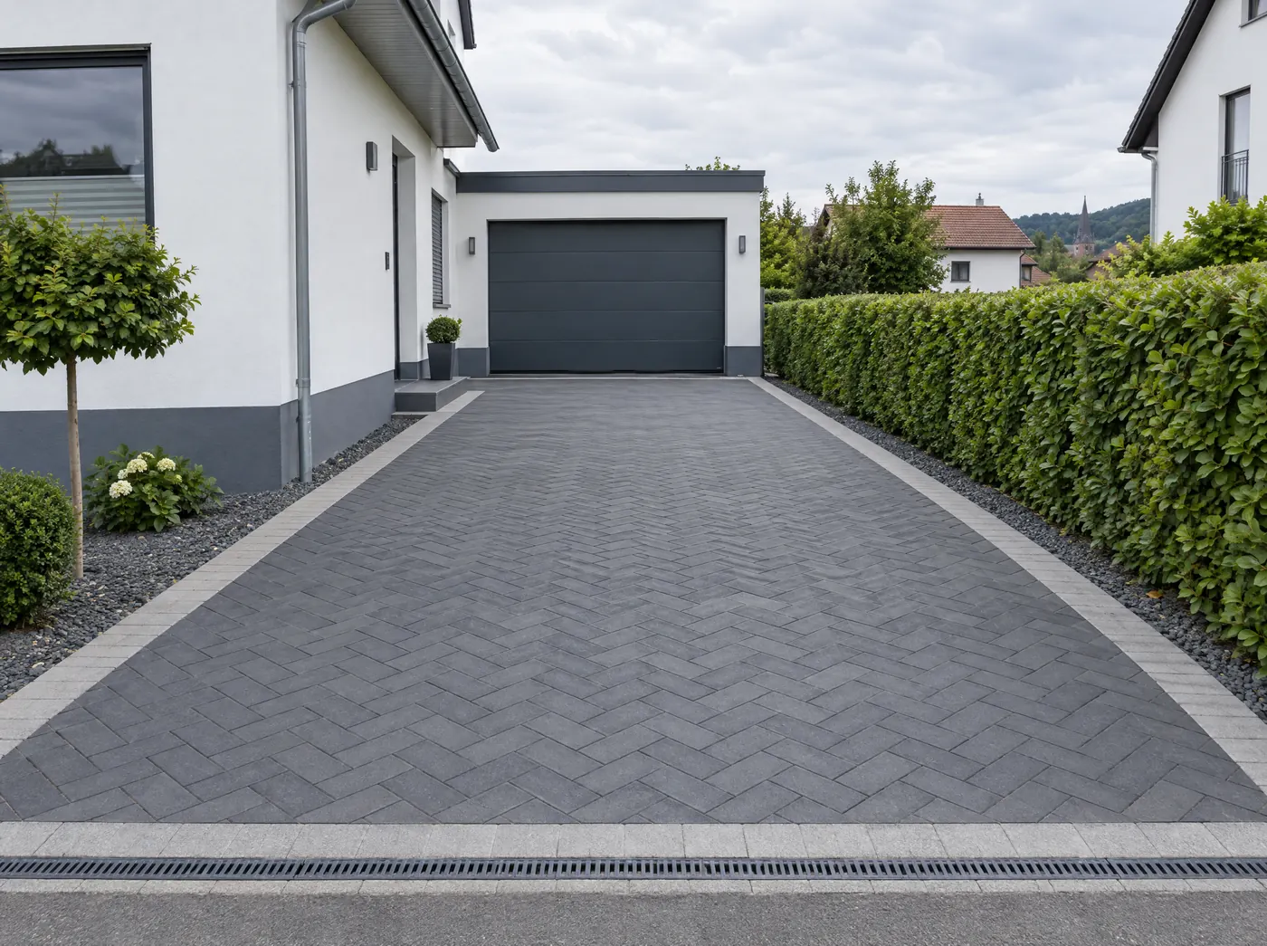 KI-Bild: gepflasterte Einfahrt in Anthrazit im Fischgrätverband mit Rinne vor der Garage